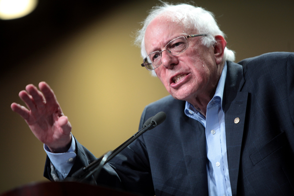 Man with unruly white hair gestures at a podium.