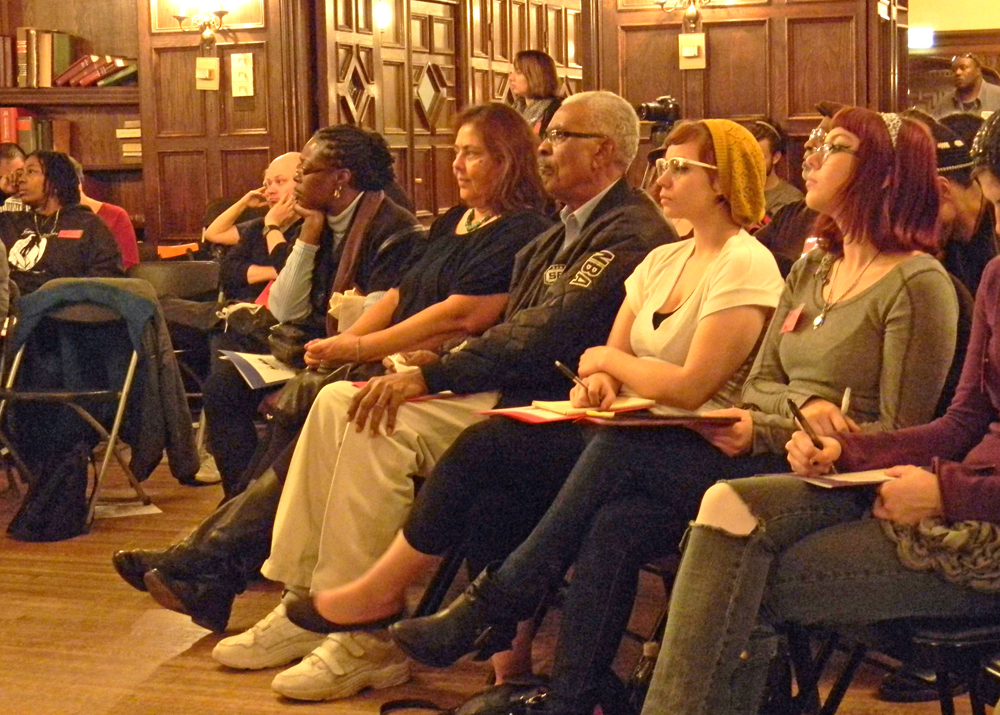 Multiracial crowd seated at a meeting pays close attention to a speaker who is out of the frame.