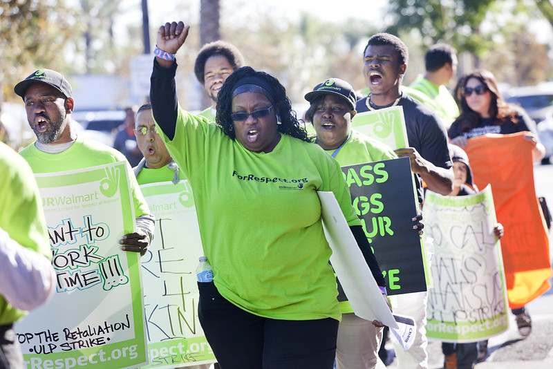 A group of marchers in green pickets Walmart with raised fists.