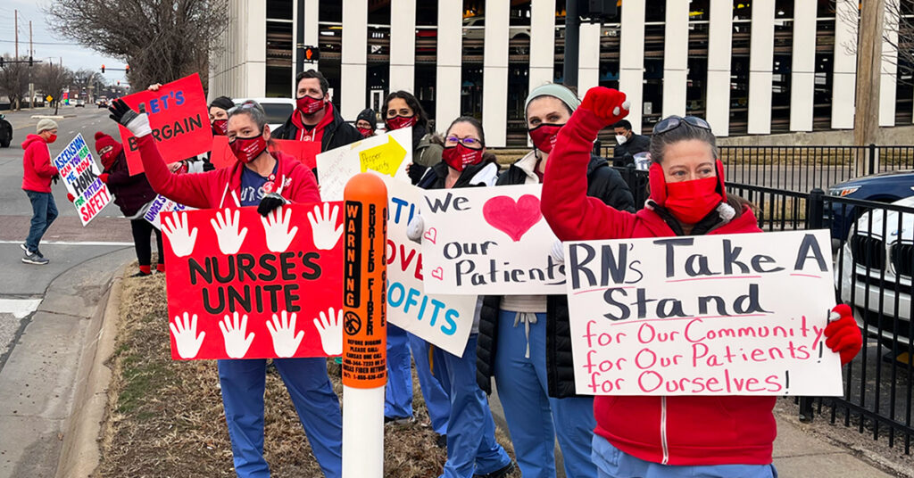 A row of nurses in red picket carrying signs reading Nurses Unite and We Love Our Patients