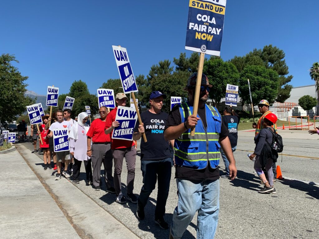 A couple of dozen picketers march holding signs reading UAW on strike