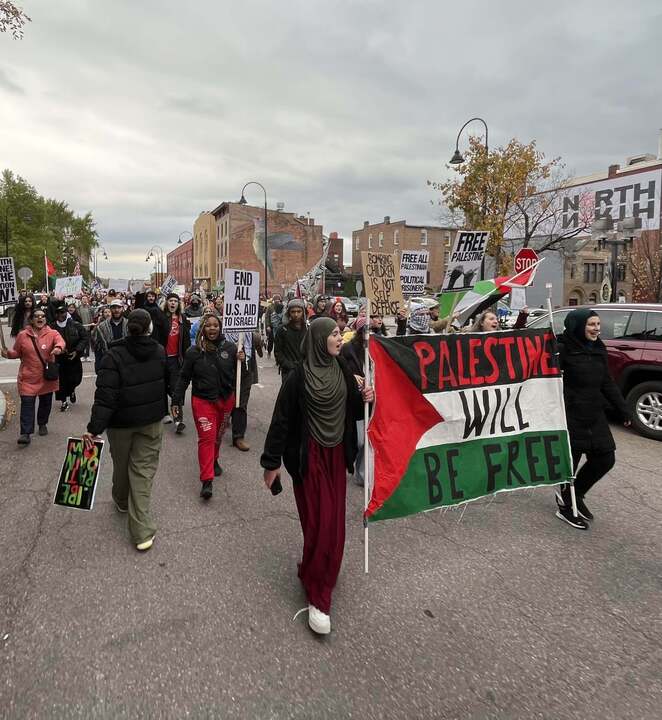 A group of people marches down a winter street behind a banner reading Palestine will be free.