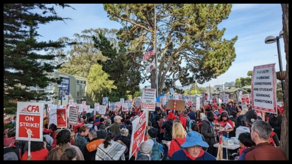 A crowd of hundreds carrying signs reading "CFA on strike!" and "Faculty working conditions are student learning conditions" is gathered on a campus plaza. Evergreen trees are in the background.