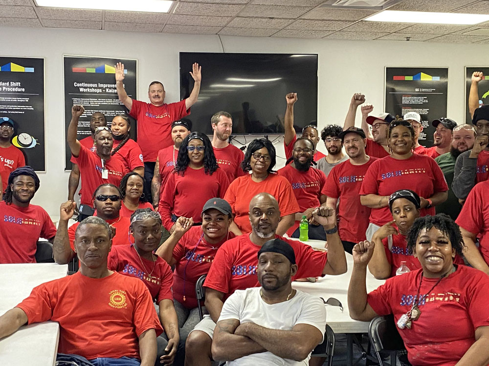 An indoor group shot of about 20 workers in red shirts that say “Solidarity.” They are sitting and standing, many of them raising fists. The crowd is predominantly Black.