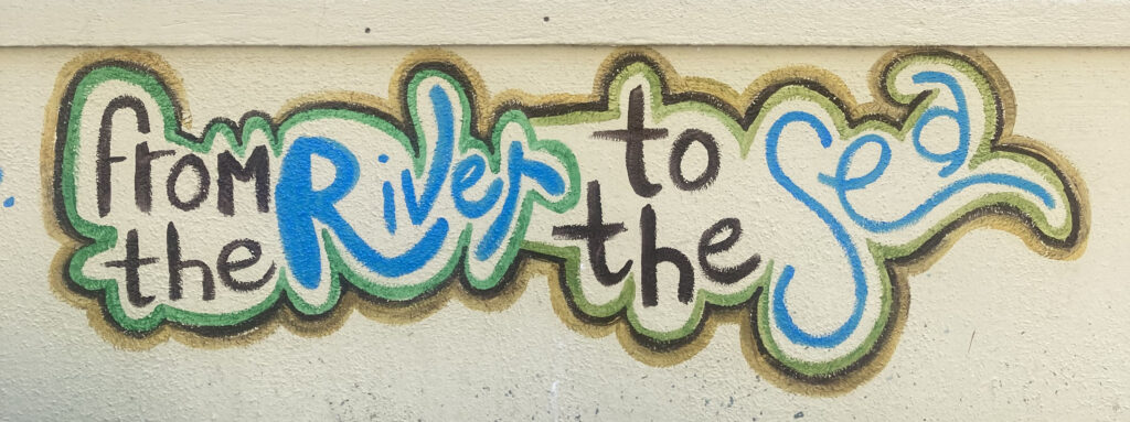 Multicolored paint on a beige wall spelling out “From the river to the sea.”