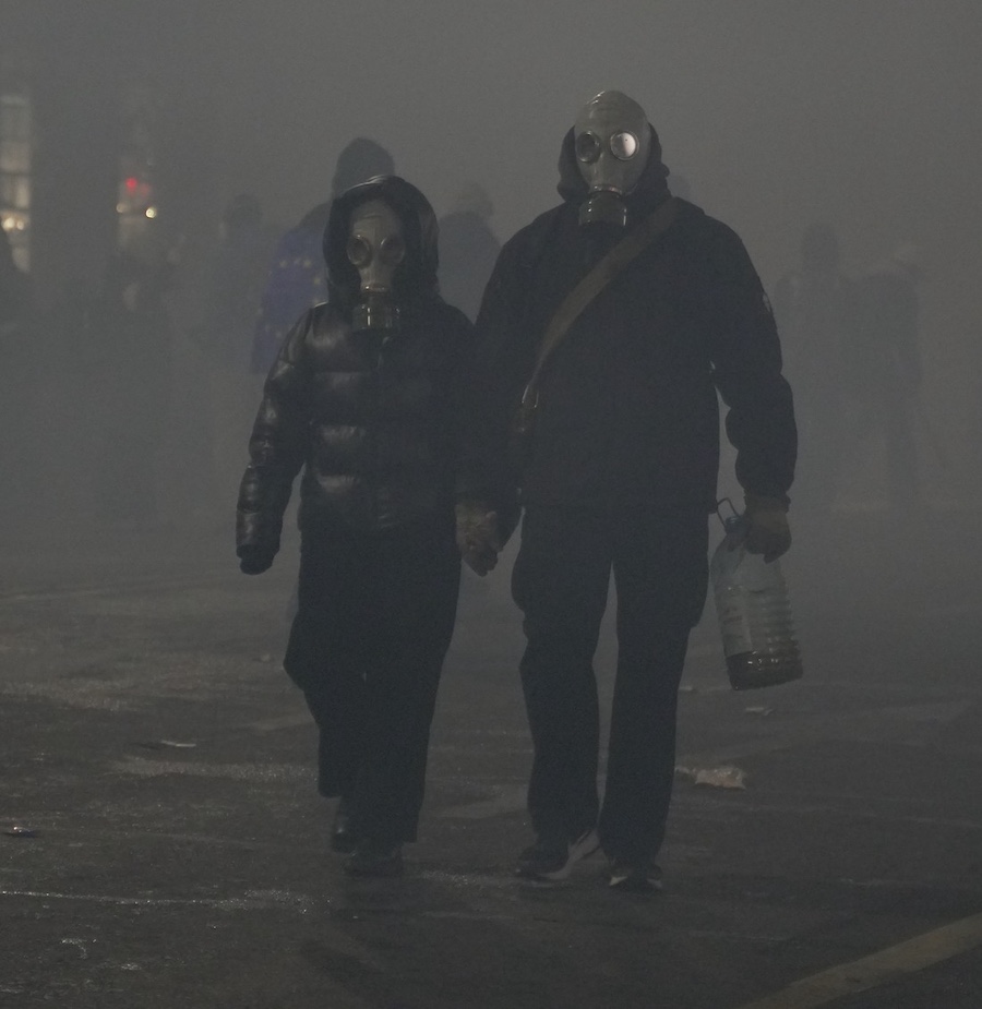 Photo from Tbilisi protest on December 3, 2024 shows two protesters, holding hands, dressed in black and wearing gas masks, surrounded by tear gas clouds Photo by Mautskebeli.