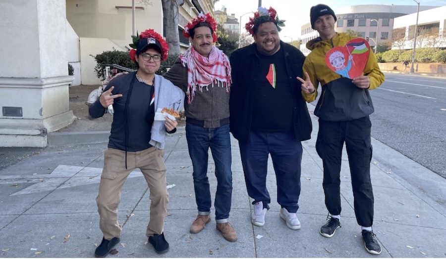 Four Palestine solidarity marchers and comrades, arm in arm. Two on either end showing peace signs, three wearing Palestine solidarity symbols. Photo by Teto.