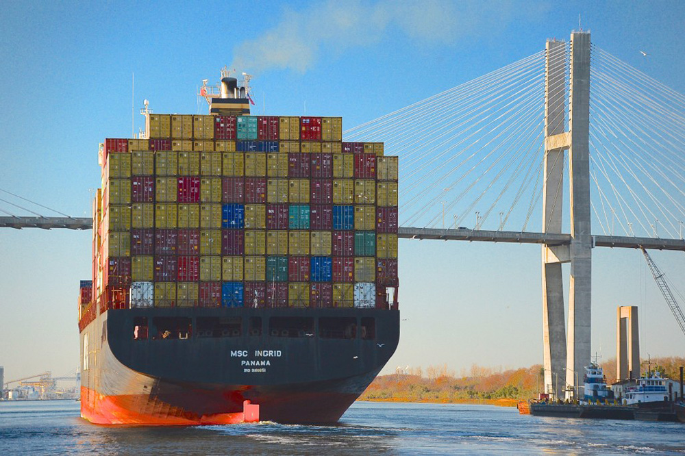 Ship full of shipping containers passes under a bridge.