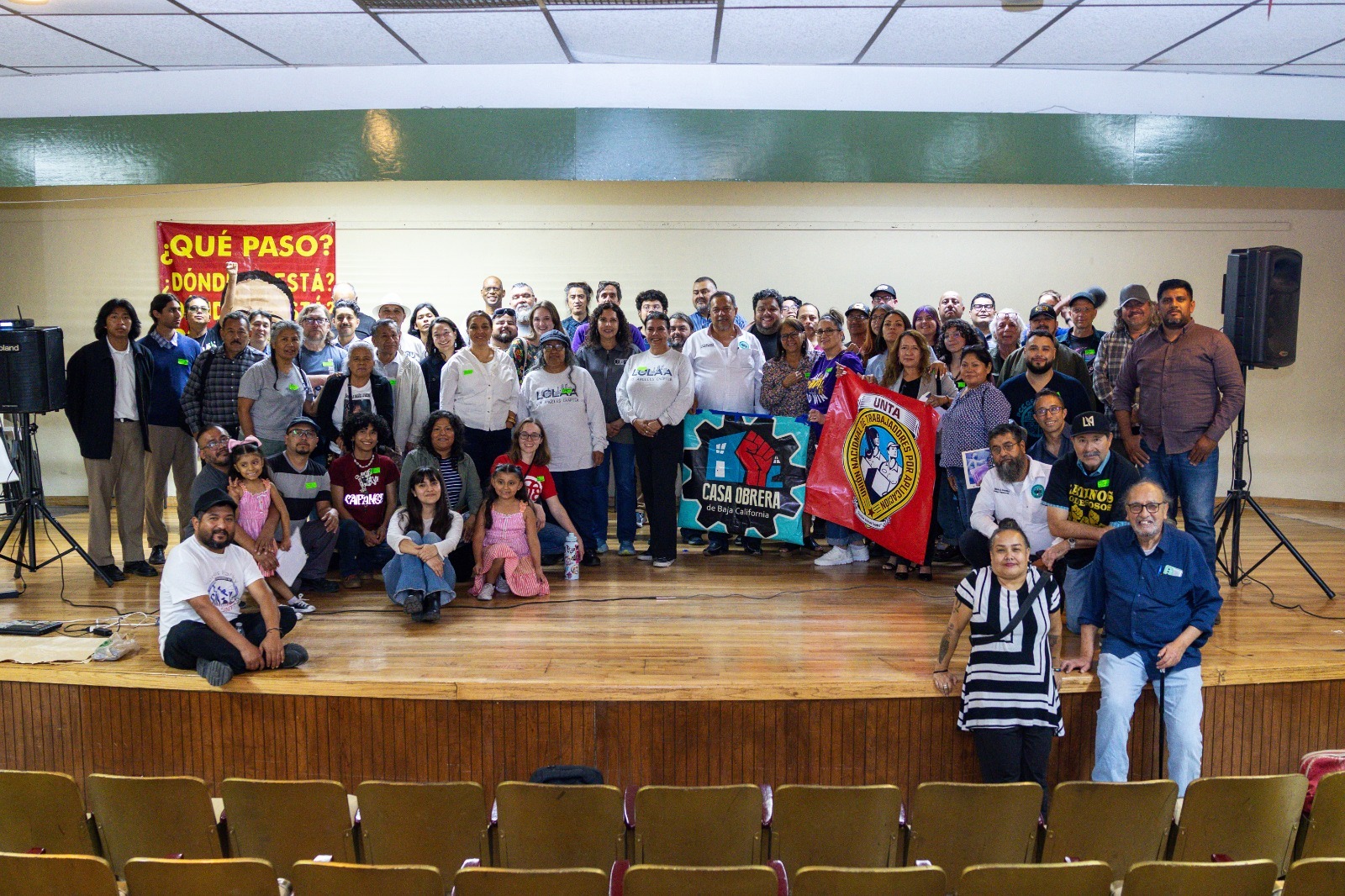 A group of people stands on a stage holding signs in Spanish.