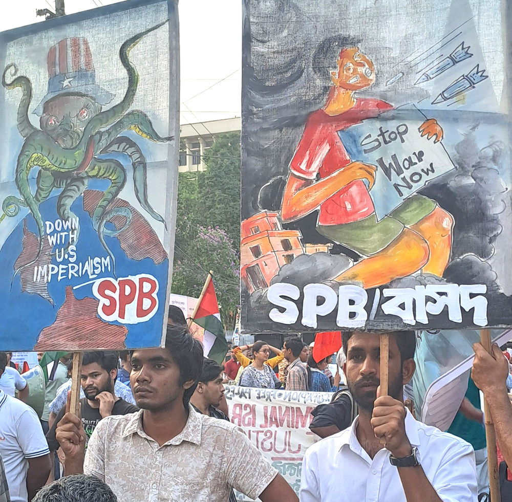 Two young men march with painted banners. On the left, the banner shows an octopus in an “Uncle Sam” hat astride the Earth, which has lettering saying “Down with U.S. imperialism. SPB.” The banner on the right shows a child facing incoming bullets and bombs and holding a sign that reads “Stop war now.”