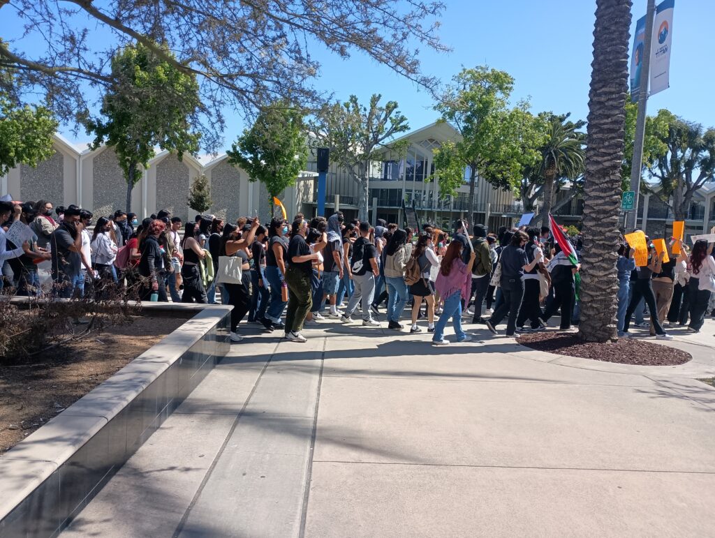 a crowd of marchers carrying Palestinian flags and signs on a university campus