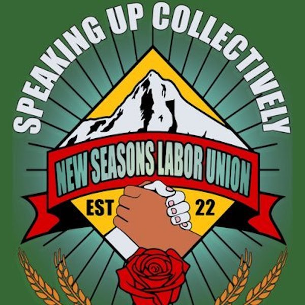 The NSLU logo which shows two hands (white and brown) grasping/ shaking in solidarity inset in diamond shaped band. A red banner reading “New Seasons Labor Union” runs across the top of the diamond witha red rose surrounded by two sheaves of wheat at the bottom.