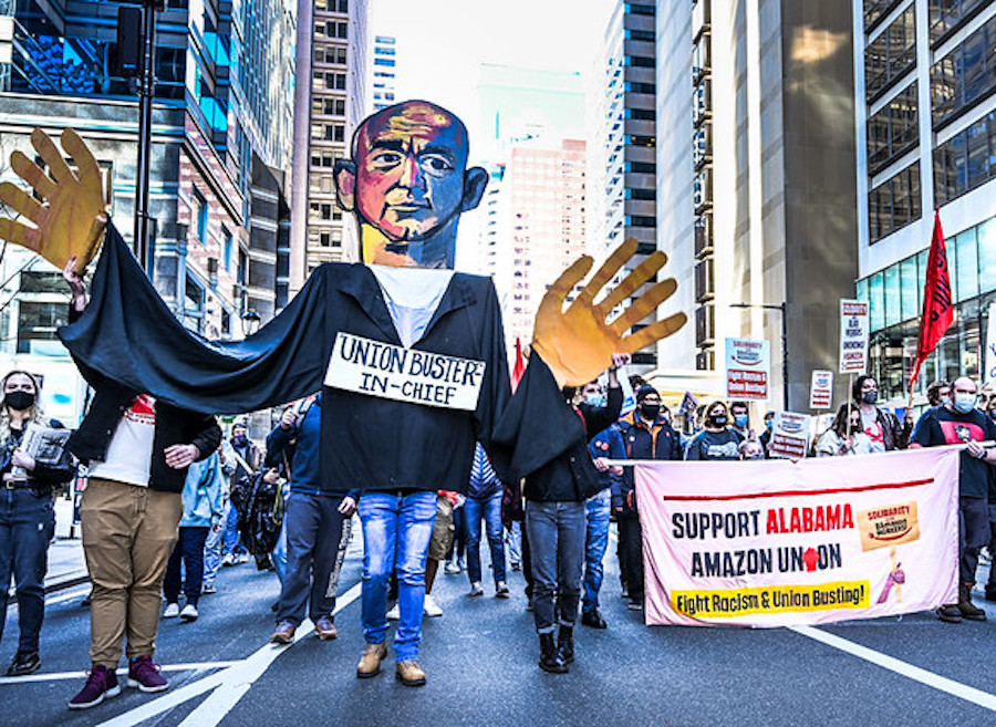 Demonstration at one of the fifty city marches in solidarity with Amazon workers in Bessamer, AL on March 20, 2021. At the front of the march is an approximate fifteen foot by fifteen foot puppet of Jeff Bezos, owner of Amazon, wearing a sign reading: “Union buster in chief.” Also, marchers carrying a solidarity banner reading: Support Alabama Amazon Union. Fight Racism and Union Busting.