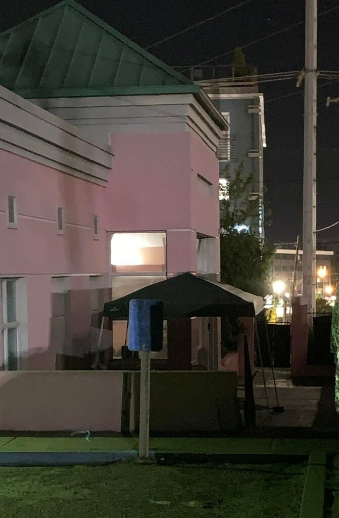 A black tent shields the patio of the two-story Pink House at night.