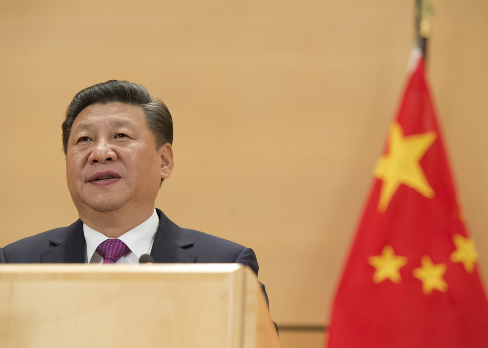A photo of Chinese leader Xi-Jinping at a podium next to the Chinese flag, red with yellow stars