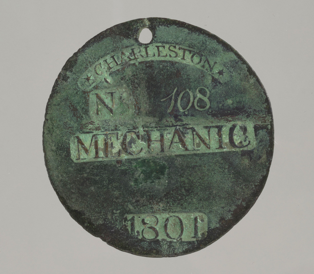 A circular copper slave badge. The front of the badge reads "*Charleston* / No 108 / Mechanic / 1801." The back of the badge reads “CPrince.” All lettering is die stamped into the metal except the number “108”, which is engraved. There is a puncture hole at the top of the badge. The metal is dark in colour with a green patina. Date: 1800s. Record ID: nmaahc_2014.118.2.URL: https://www.lookandlearn.com/history-images/YSH000898/Charleston-slave-badge-from-1801-for-Mechanic-No-108?t=1&q=slave+badge&n=5