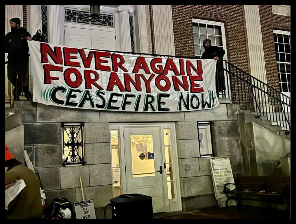 Photo of a banner used at a protest of U.S. Representative Becca Balint’s fundraiser on November 9, 2023. The banner reads, “Never Again for Anyone”, in red, and “Ceasefire Now”, in black, on a white banner. Photo taken by comrades.