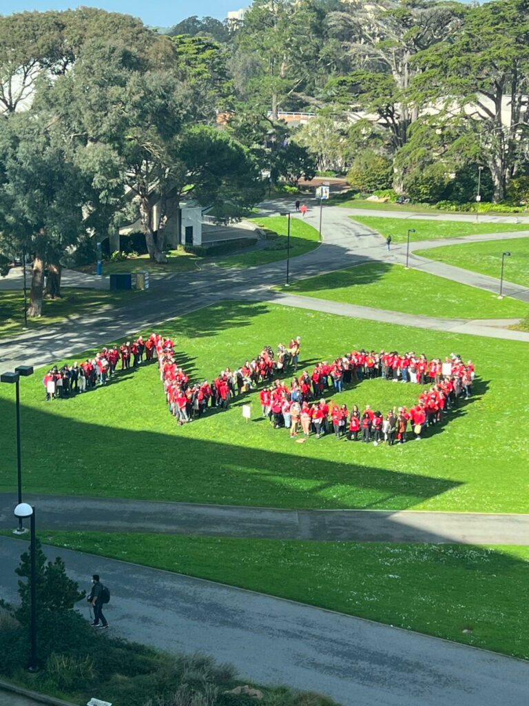 A few hundred activists wearing red spell out the word NO on a lawn at SF State University.
