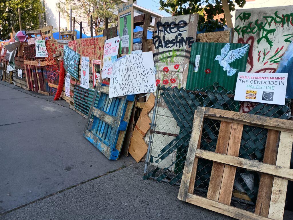 A row of signs and artwork outside an encampment of tents at Cal State LA