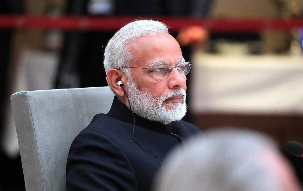 Seated man with neatly-trimmed white hair and beard listens through an earpiece to translations at a meeting.