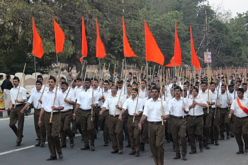 Men march in formation in the streets in white shirts and Khaki pants, carrying clubs and red flags.