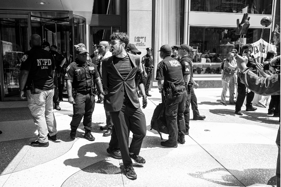 Police arrest an anti-EACOP activist in New York in a black and white photo of a street scene of protest.