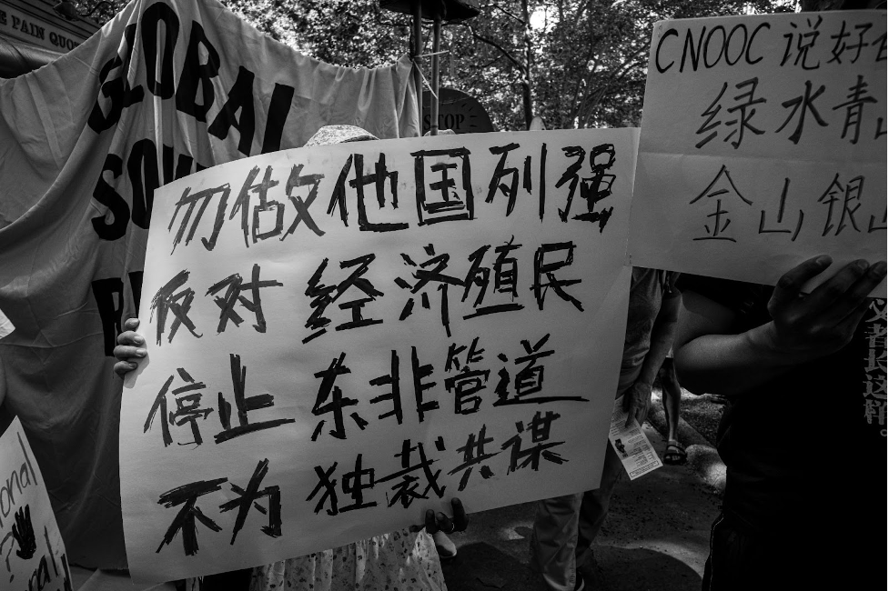 The sign reads: “Do Not Be an Imperialist Power. Against Economic Colonialism. Stop EACOP. No Collaboration With Dictatorships.”