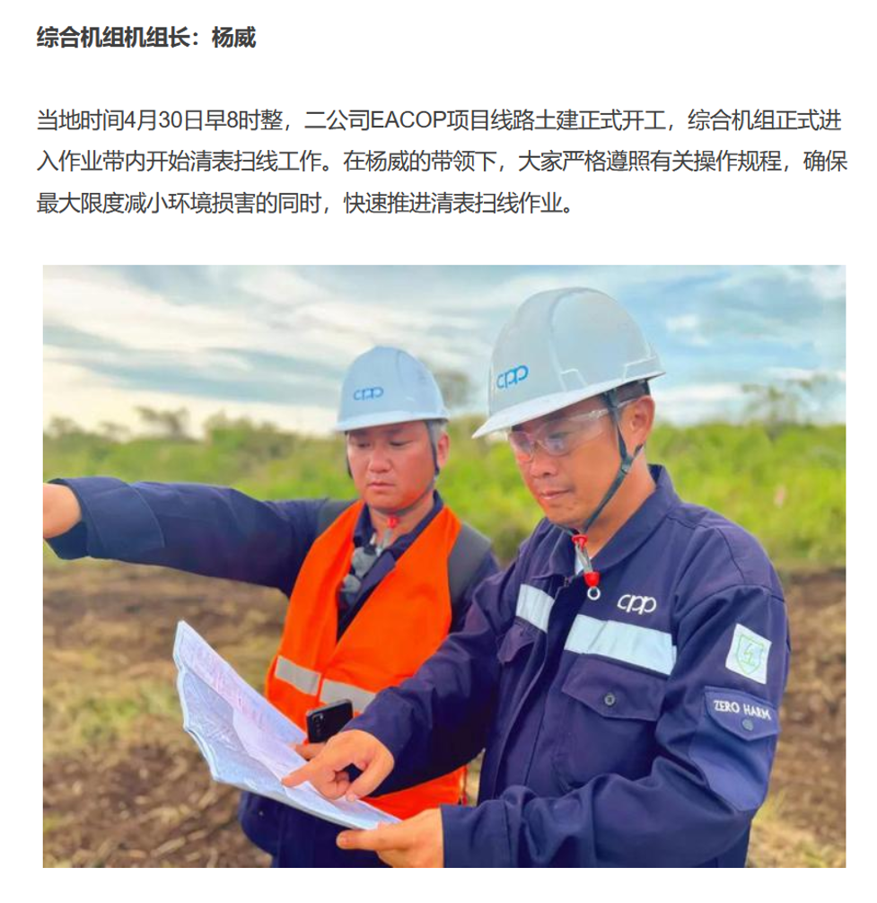 Two people  in blue jumpsuits and hard hats examine a map or document.