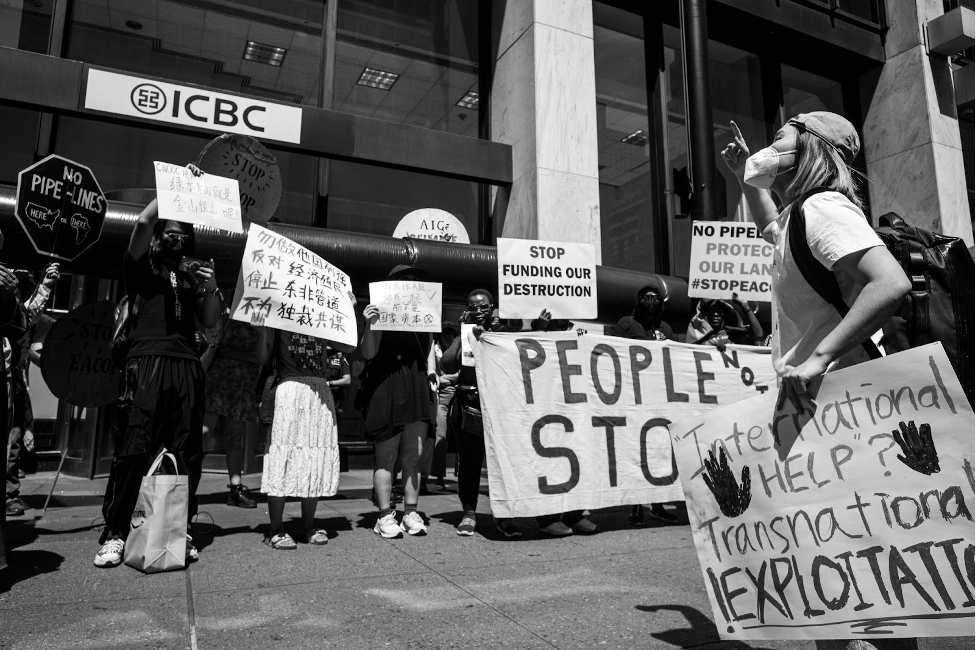 Protesters in front of ICBC. Black and white photos. Signs in both Chinese and English, two reading “Stop Funding our Destruction,” and “No pipelines.”