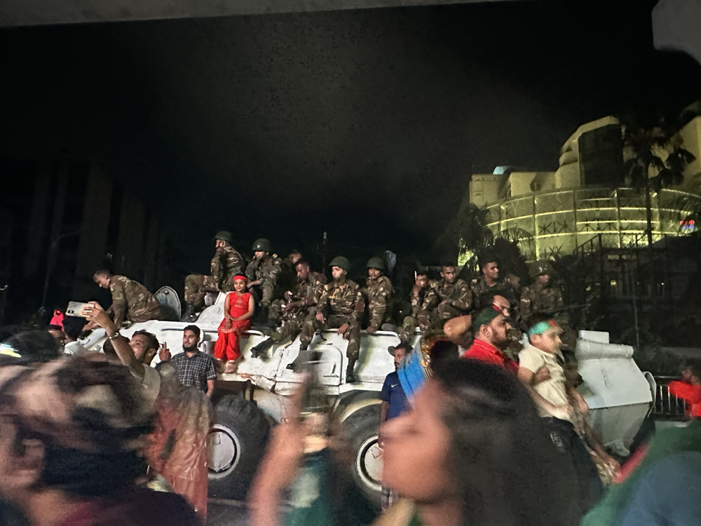 Nighttime shot of crowds around a large army vehicle. Soldiers and civilians are relaxed.