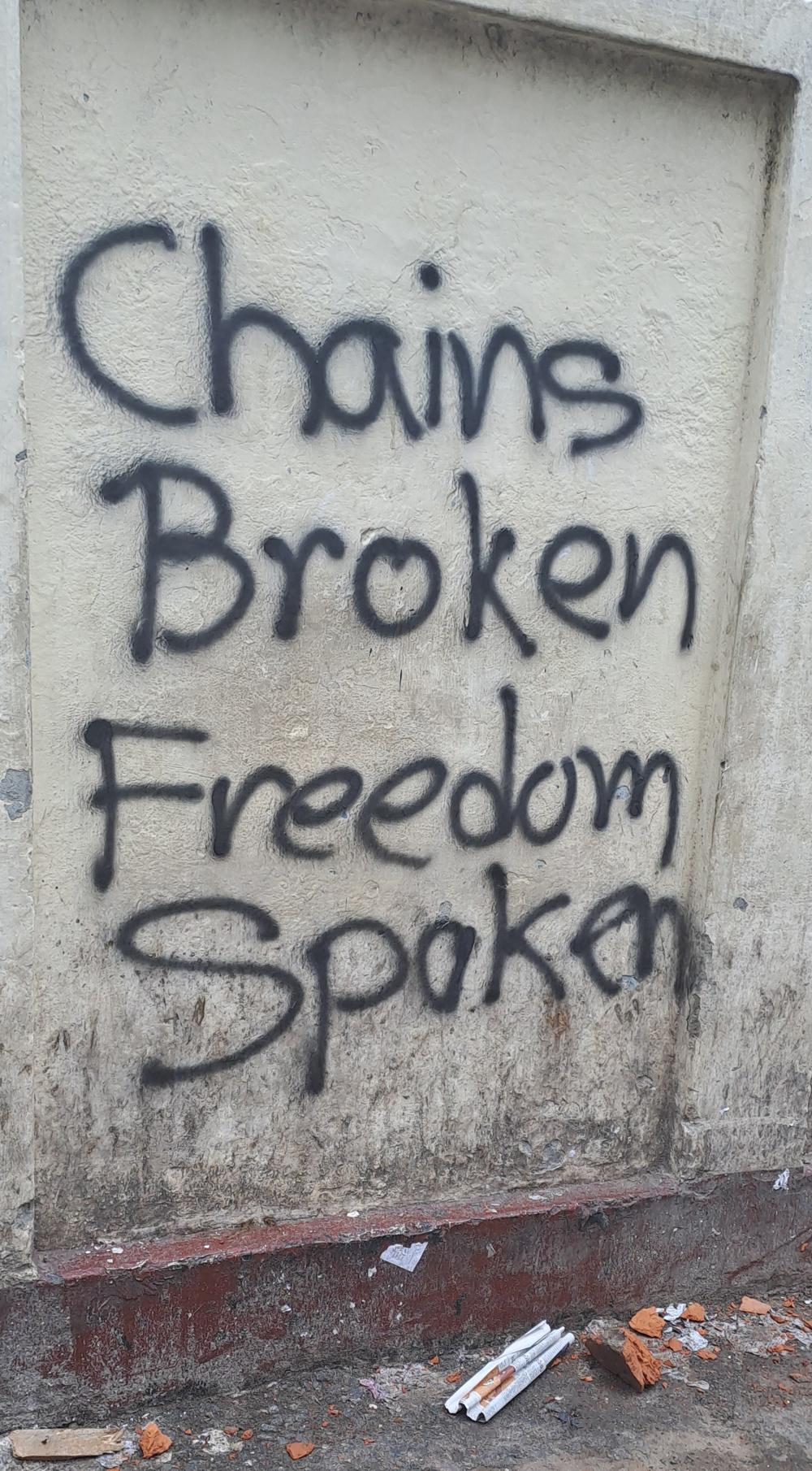 Black graffiti on a dirty white wall says, “Chains broken freedom spoken.”