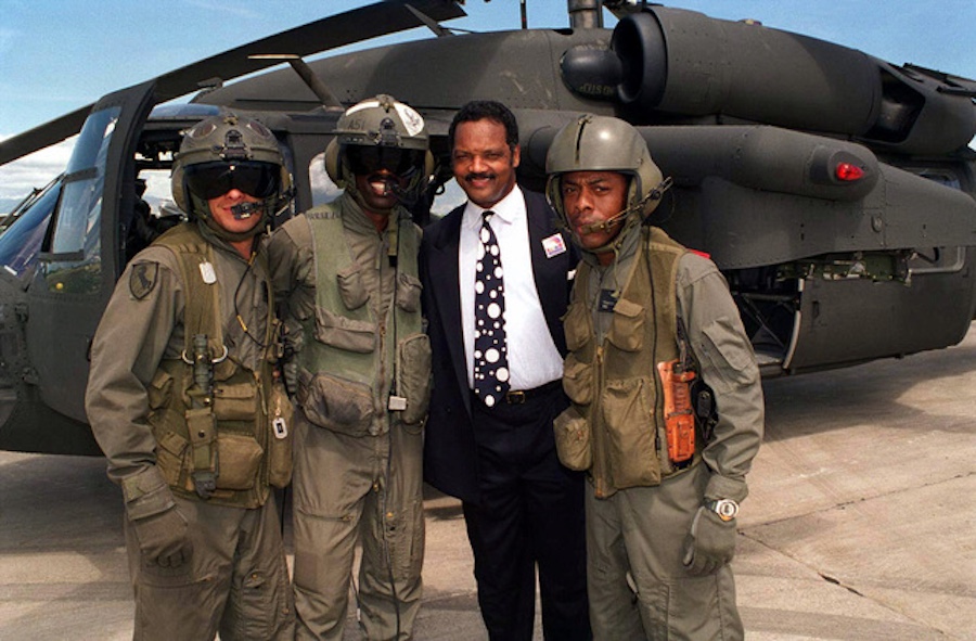 Photograph shows the Reverend Jesse Jackson, leader of the Rainbow Coalition, in October 1994, alongside three uniformed members of the 3-25 Aviation Battalion, 10th Aviation Brigade, 10th Mountain Division, Light Infantry, posing in front of an AH-64A Apache helicopter outside the Port au Prince International Airport after the Marine invasion of Haiti, part of Operation Uphold Democracy. Photo by the Collection - US Marine Corp.