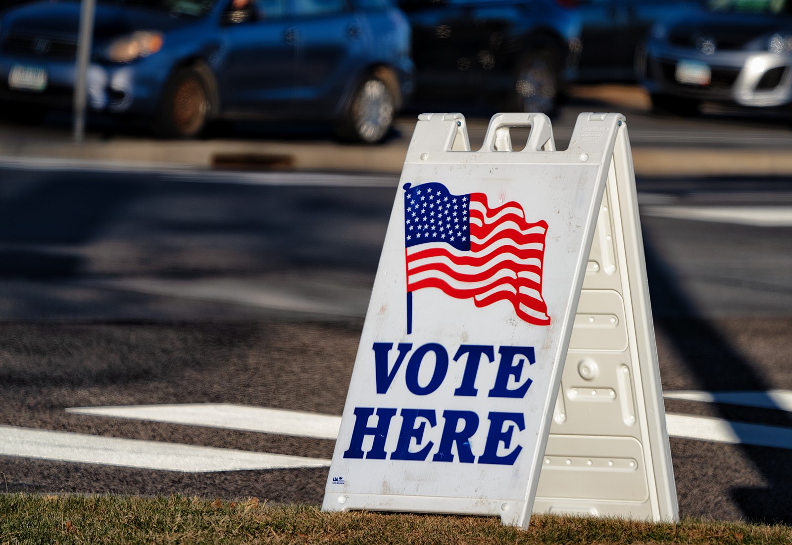 A plastic sandwich sign saying Vote Here in red, white, and blue.