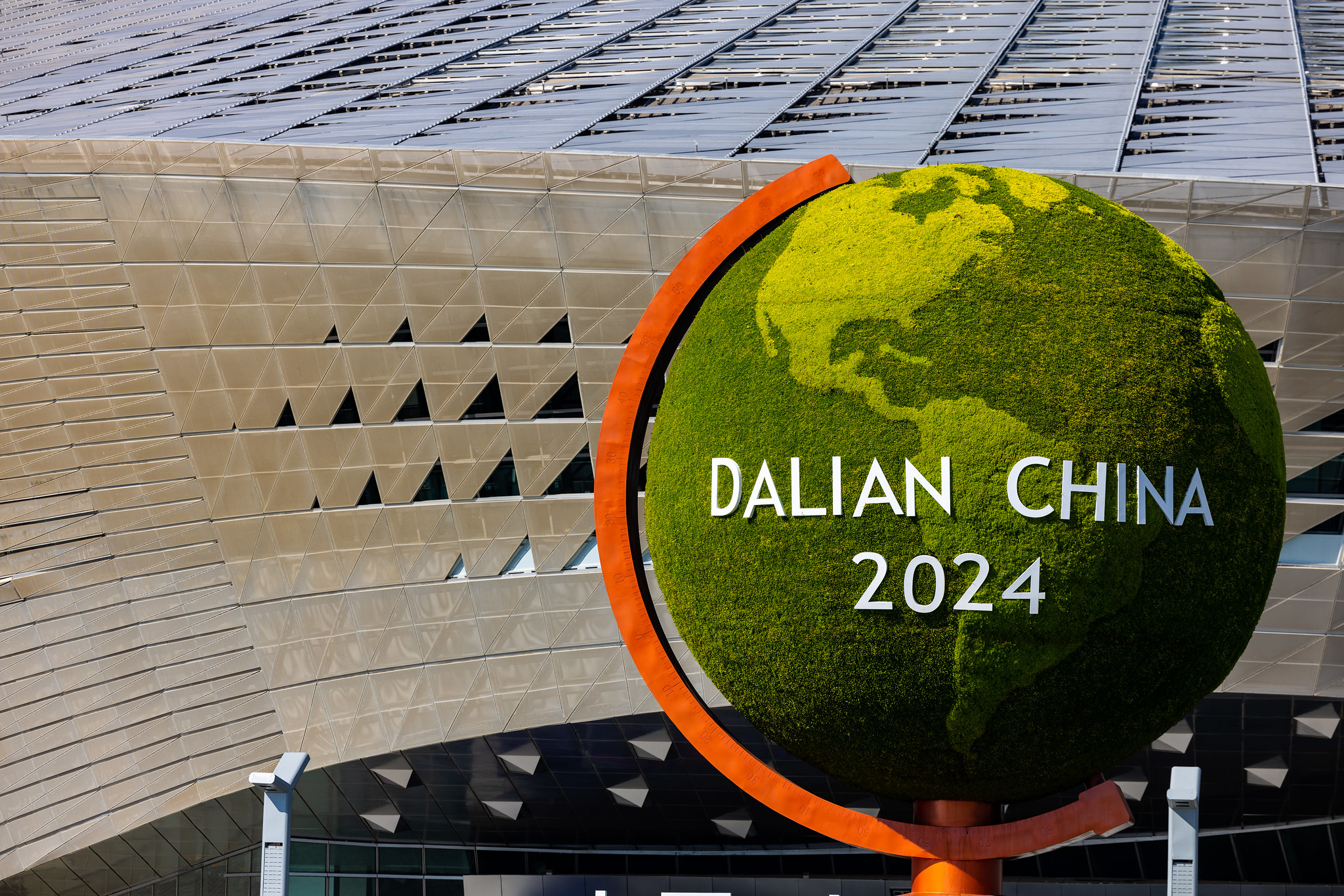 A large green globe with DALIAN CHINA 2024 written on it, in front of a building.