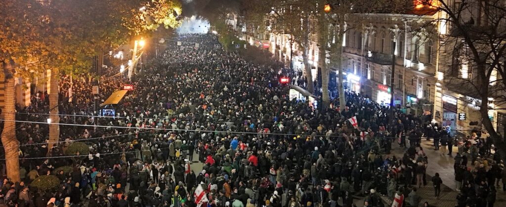 Photo of mass demonstration in Tbilisi, December 5, 2024, which shows thousands in the streets with tear gas clouds in the background. Photo by Mautskebeli. 