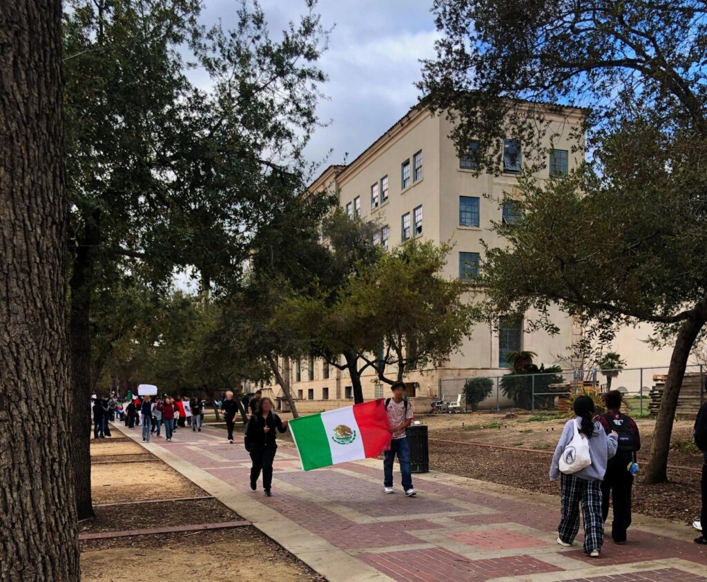 John Muir Students Arriving for the Pasadena Protest. Photo shows two students in foregorund marching and carrying a Mexican flag. 