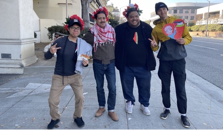  Four Palestine solidarity marchers and comrades, arm in arm. Two on either end showing peace signs, three wearing Palestine solidarity symbols. Photo by Teto. 