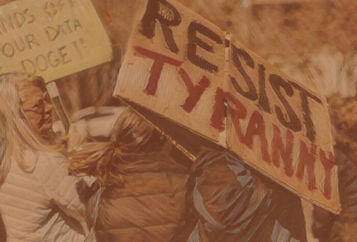 A picture of a sign in a protest crowd with "resist tyranny" written on it.