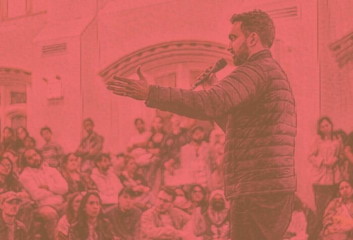 A photo of Zohran Mamdani addressing a crowd on a microphone, covered with a red filter.