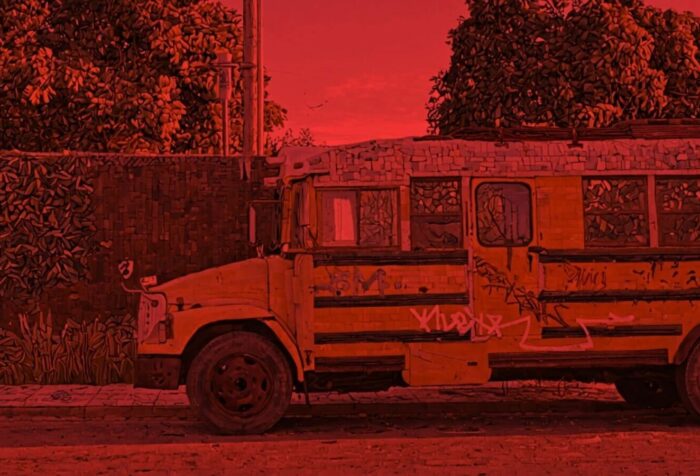 A red-filtered photo of a school bus facing left on a street in front of a wall and trees.