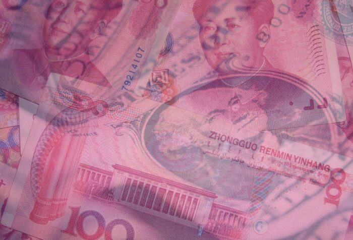 US dollar bills and Chinese yuan bills overlap. A pink filter over the image.