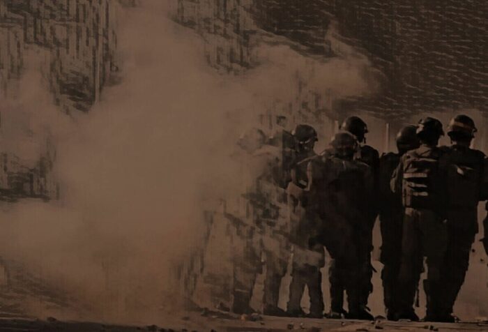 A militarized group of police stands while tear gas floats to the left.