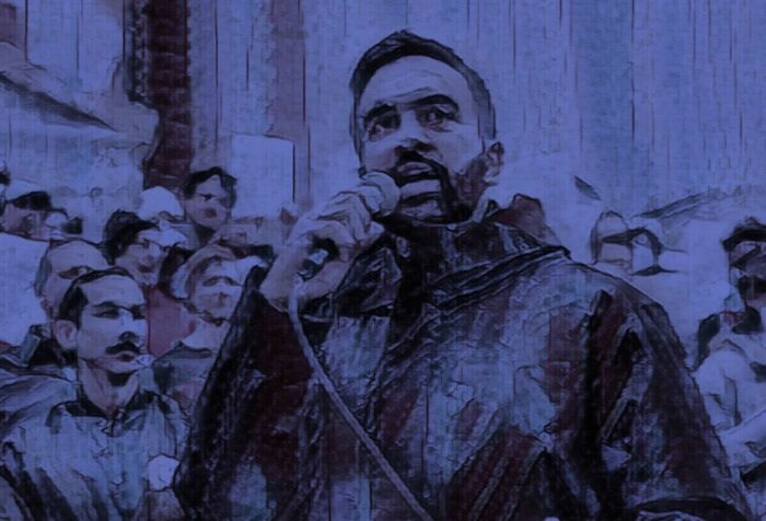 Foreground: Bearded young man speaks speaks outdoors into a microphone. Background: Rally-goers hold signs and listen as they stand on the steps of a building with large columns. A blue tint filter over the whole photo.