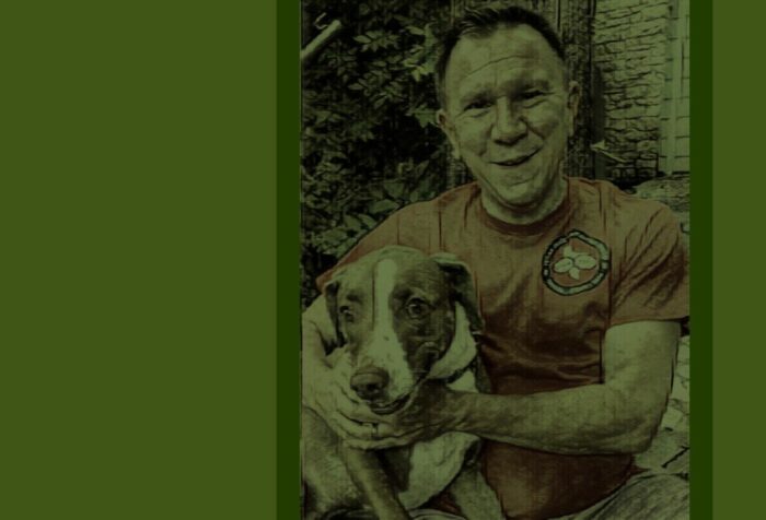 A photo of Tom Alter smiling at the camera holding his dog. The photo has a green filter over top of it.