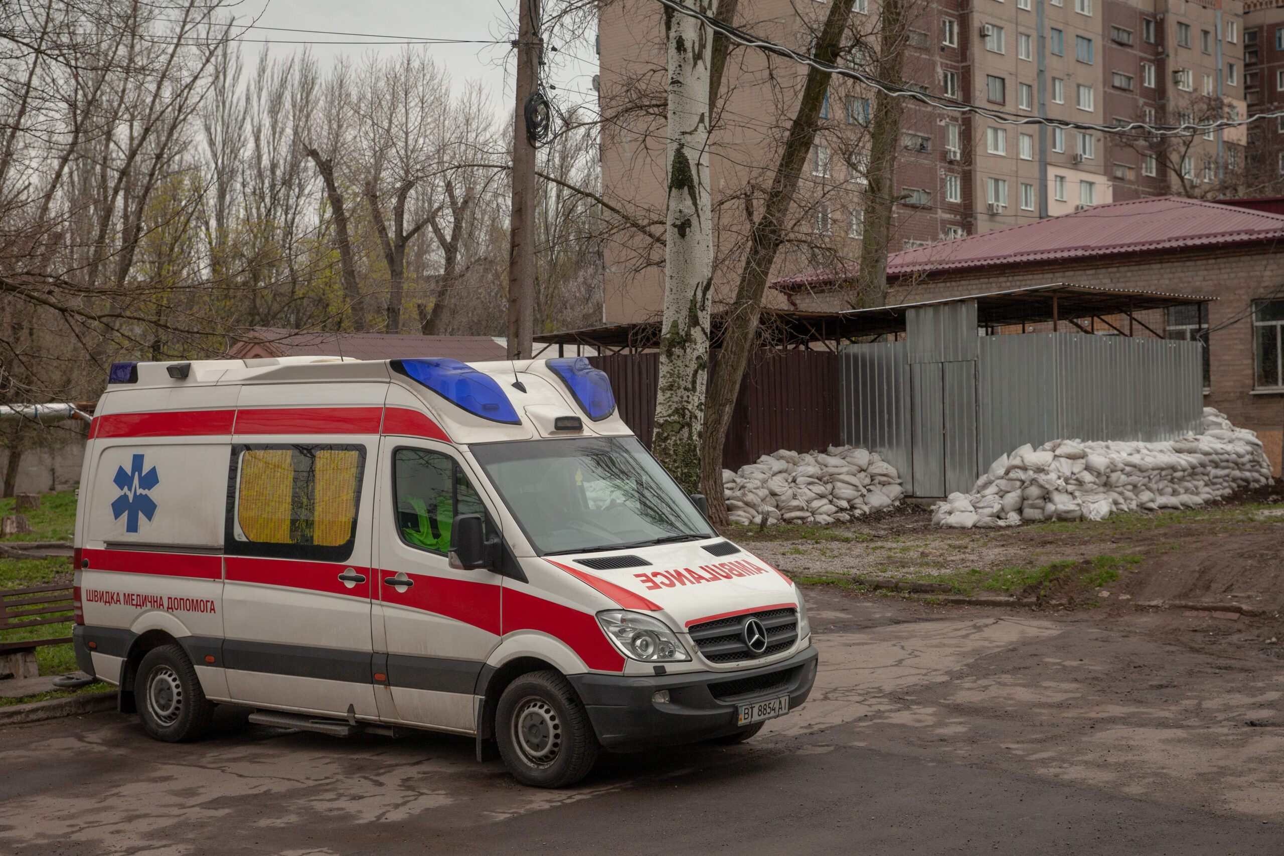 A photo of an ambulance parked in front of bare trees and buildings.