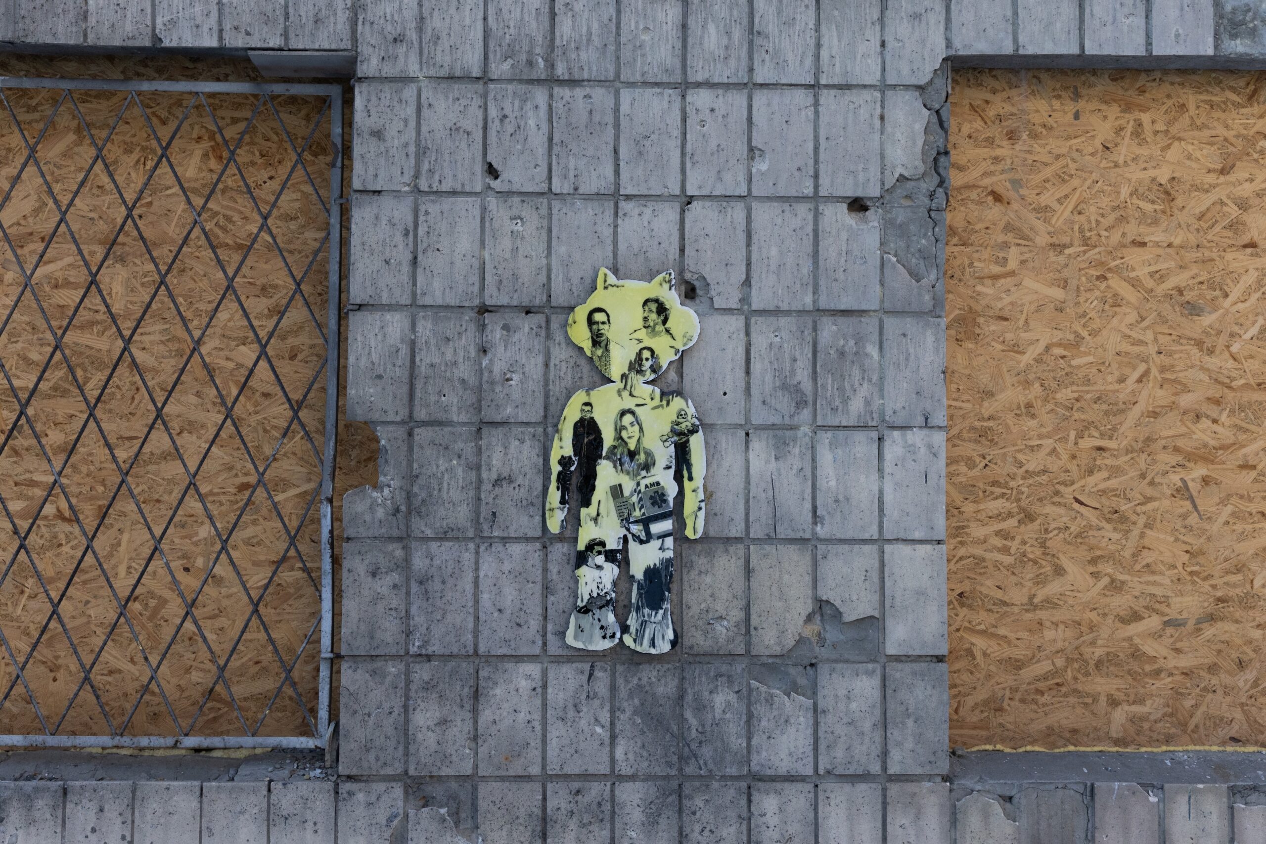 A photo of a concrete wall. Hanging on it is a mural, a human figure shape with photos of nurses on it.