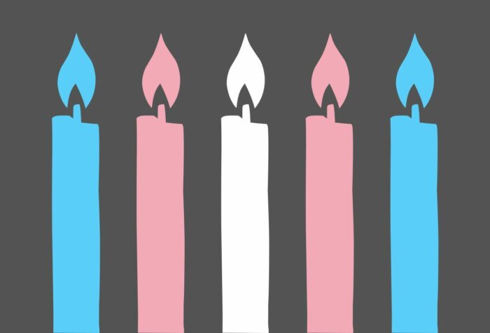 Against a dark grey background are 5 candles in the colors of the trans flag stripes (blue, pink, white, pink, blue) from left to right.