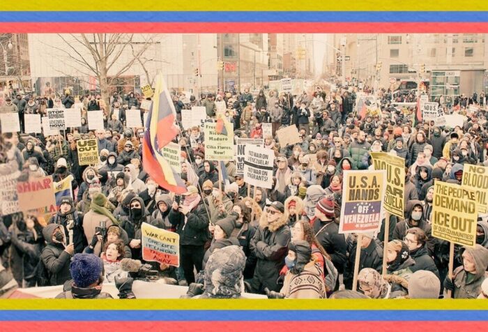 A photo of a protest crowd with signs such as "USA Hands off Venezuela" and "The People Demand ICE out of our communities." Across the top and bottom of the photo are a banner of yellow, blue, and red stripes of the flag of Venezuela.