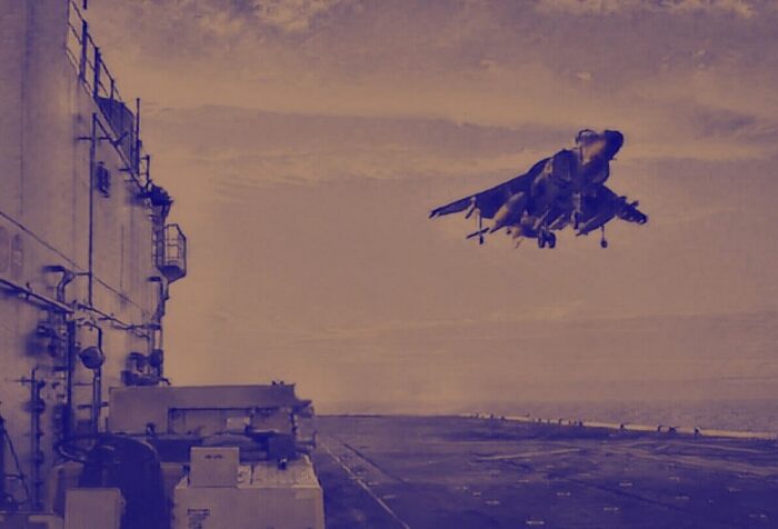 A photo of a fighter jet in the air landing on the flight deck of a ship.