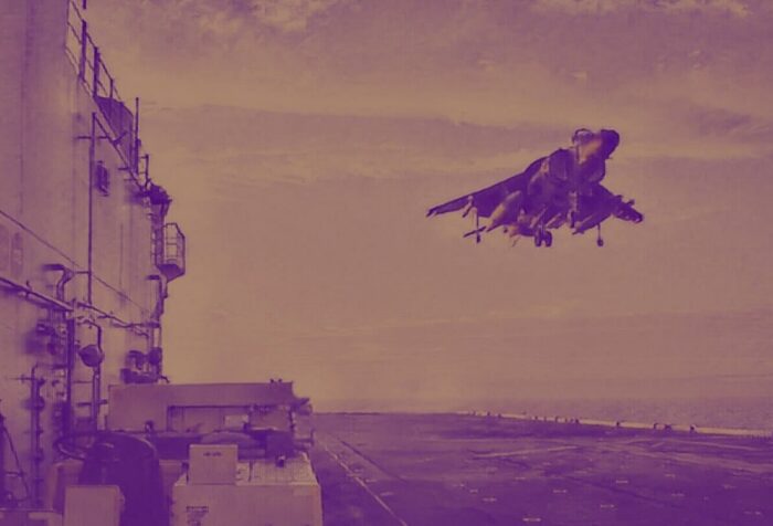 Una foto de un caza en el aire aterrizando en la cubierta de vuelo de un barco.